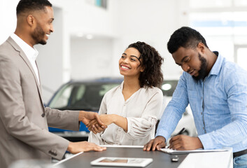 Buying Car. Black Couple Shaking Hands With Salesman And Signing Papers In Cars Selling Center. Selective Focus