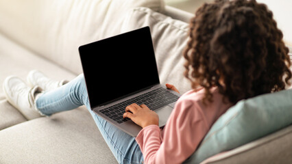 E-learning. Over shoulder shot of schoolgirl looking at laptop with blank screen, having video call with teacher or tutor, online studying during pandemic. Teen sitting on sofa at home