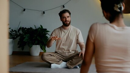 A male yoga mentor talks and gestures while a female student sits across from him