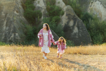 Fototapeta premium A young mother and daughter are walking in nature among the mountains in beautiful identical sweaters