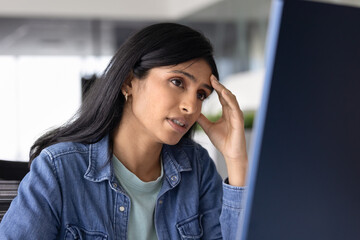 Tired young Indian product manager woman working at computer monitor, touching head, thinking on career problem, work mistake, getting bad news, watching or reading content