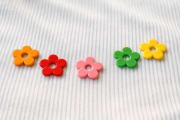 Brightly colored flower form plastic trim against a blue and white cloth under daylight