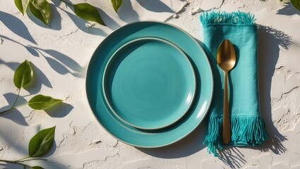 Vivid turquoise plate paired with a fringed napkin on a smooth white background, accented by leaf shadows, ideal for spring or summer dining decor. Copy space available.