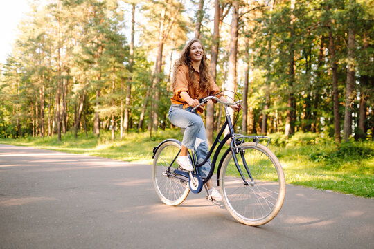 Young woman riding a bicycle on a path in a dense sunny forest. Happy woman enjoying nature and cycling at sunset. Weekend concept. Active lifestyle.