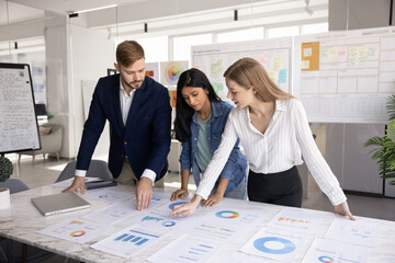 Marketing agency diverse workers analyzing research results, paper reports with diagrams on meeting table, discussing business startup creative strategy, planning finance, expenses, profit