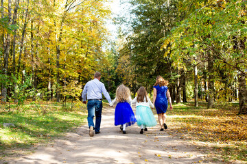 Fototapeta premium Family with children walking hand in hand along a forest path in autumn.
