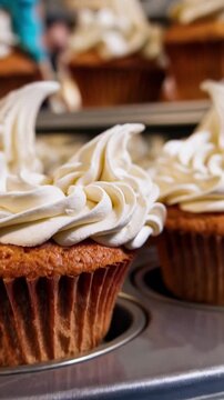 Close up of a pastry chef skillfully decorating multiple cupcakes with creamy white frosting, creating visually appealing swirls and patterns using a piping bag