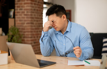 Naklejka premium Mature male entrepreneur suffering eyes strain, taking off glasses and massaging nose bridge, feeling tired after working on laptop computer at home office, free space