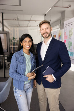 Two happy young multiethnic business colleagues posing for business portrait. Positive diverse coworkers looking at camera, standing together, enjoying teamwork, collaboration, office friendship