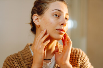 Close-up reflection of young woman in mirror doing skin care in bathroom. Beautiful woman touching...
