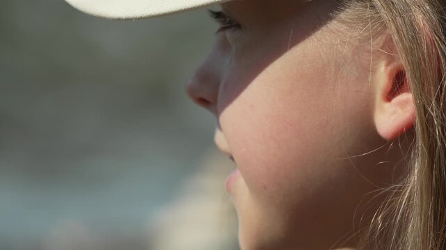 Girl speaking profile, young teen with braces wearing a white baseball cap outdoors.