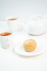 A single, golden sesame ball rests on a plate, presented with a teapot and two cups of warm tea for a simple and inviting moment of refreshment.