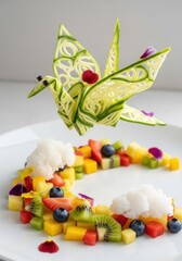 Photo of an elegant fruit platter with a delicate cucumber origami crane perched above a colorful arrangement of fresh fruits like strawberries, blueberries, kiwi, and pineapple.