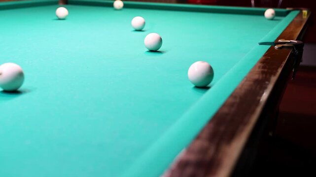 A person plays billiards, hitting a white ball with a cue stick on a green table