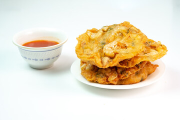 
Description:
A stack of golden-brown bakwan udang, an Indonesian shrimp fritter, sits on a white plate next to a small bowl of sweet chili dipping sauce, a popular street food snack.