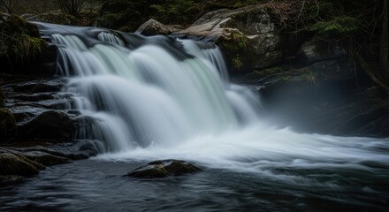 Fototapeta premium Cascading waterfall spills over dark rocks
