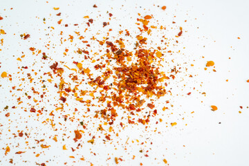 A close-up, macro shot of red chili flakes and spices scattered across a white background,...