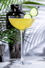 Enjoy cucumber gimlet cocktail drink with gin, syrup, lime juice and cucumber wheels. Marble table in elegant lounge with palm leaves