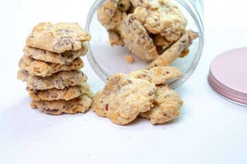 A plastic jar of almond cookies has tipped over, with a stack of cookies neatly arranged to the side. The scene highlights the delicious, crunchy treats and the jar's rose gold lid.
