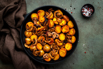 Fried potatoes with mushrooms in frying pan. Rusty green background, top view