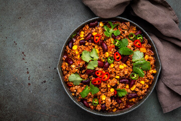 Mexican meet Chili with beef, beans, paprika, corn, cilantro, jalapeno in tomato sauce, in frying pan, rusty green background top view