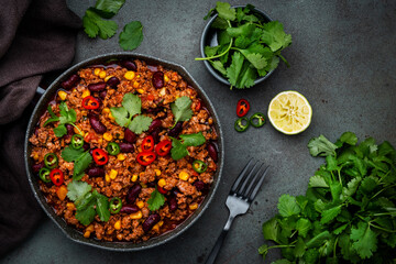 Chili con carne with beef, beans, paprika, corn, cilantro, jalapeno in tomato sauce, in frying pan, rusty green background top view