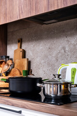 Steel pots on induction hob and kettle on cozy modern kitchen with cooking utensils, pots, cutting boards on wooden countertop