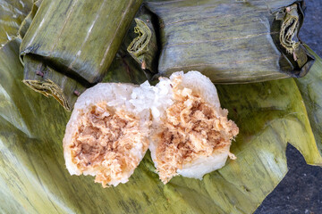 A close-up shot of Lemper Ayam, a traditional Indonesian savory snack. It features sticky rice filled with seasoned shredded chicken, wrapped and steamed in banana leaves, with one piece cut open 