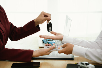 A car salesman hands over keys to a customer, symbolizing agreement, contract, purchase, rental, or insurance, representing finance, business, ownership, transportation, dealership service, and succes