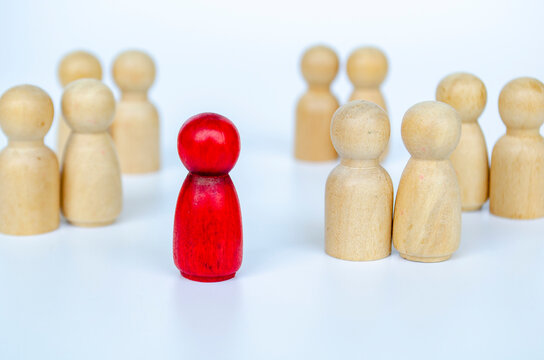 A red figure isolated from the other wooden group, representing leadership or exclusion or discrimination concept