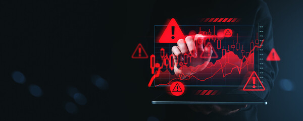 Financial crisis warning concept with hand touching digital chart showing red alert symbols and falling stock market data on dark background.