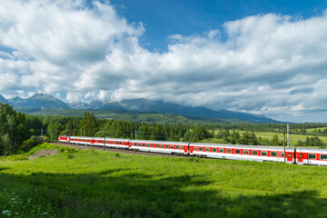 Red and white train passing through green valley in Slovakia near High Tatras mountains