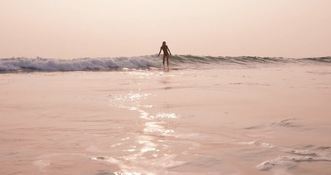 Surfer woman riding on longboard in ocean on small fun wave with sunset sun light.