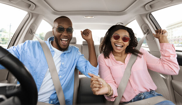 Yes, Summer Vacation Concept. Portrait of excited playful black couple in sunglasses driving car, shaking fists dancing to music enjoying favorite playlist, resting on weekend, windshield view - Powered by Adobe