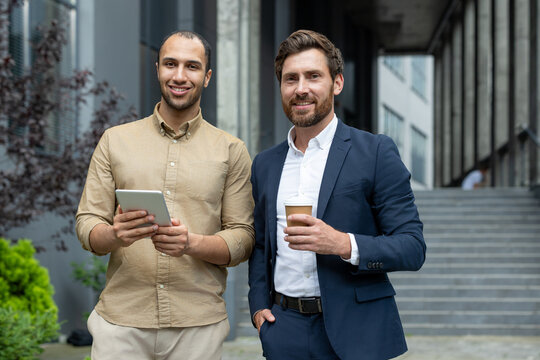 Colleagues collaborating outdoors, discussing projects while holding a tablet and coffee cup. Emphasizes teamwork, professionalism, and the use of technology in a modern urban environment.