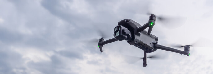 A drone ascends gracefully into the sky, soaring above a dynamic landscape filled with clouds. Its propellers spin rapidly while capturing breathtaking aerial views of the surroundings.