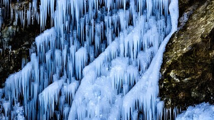 Icy cascades of a frozen waterfall in a winter mountain landscape, surrounded by frost-covered rocks and trees