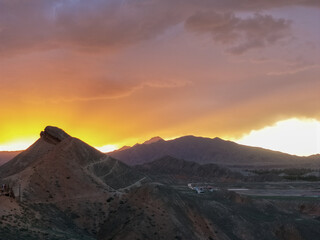 Sunset over mountain peaks in Zhangye National Geopark,China,orange sky glowing behind silhouette hills,dramatic dusk light,nature background,peaceful travel scenery