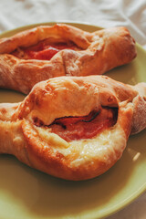 Baked Greek peinirli stuffed with melted cheese and slices of cured meat on a green plate.