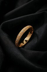 A gold bangle with intricate designs resting on a black satin fabric creating a luxurious display
