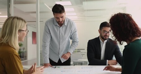 Group engaged in collaborative decision-making in meeting room, reviewing charts and diagrams spread out on conference table, analyze visual data, discussing key metrics, develop data-driven strategy - Powered by Adobe