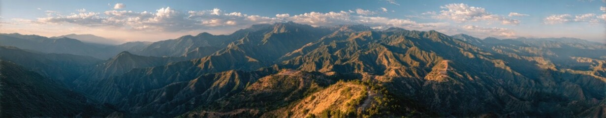 Panoramic view of a mountain range at sunrise or sunset.  Misty, layered peaks stretch across the image.  Soft light bathes the landscape