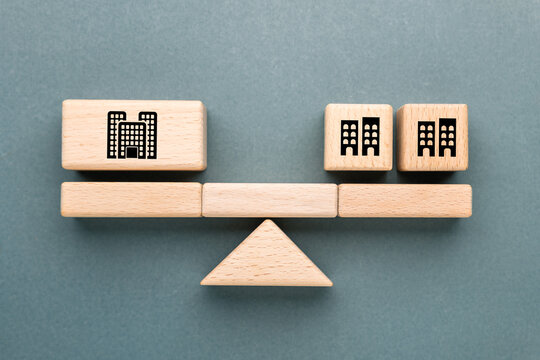 Wooden blocks on balance scale showing one big company versus several small companies, concept of spin off, business comparison, corporate strategy, growth potential