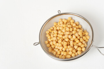 Raw, washed chickpeas. Stored in a metal colander inside a white bowl. On a white background. Ready to prepare any delicious recipe.
