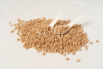 On a handful of chickpeas, two white ceramic spoons. All on a white table.