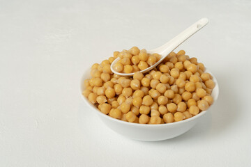 Boiled chickpeas. In a white bowl with a white porcelain spoon. On a white background. Ready to complement any delicious recipe.