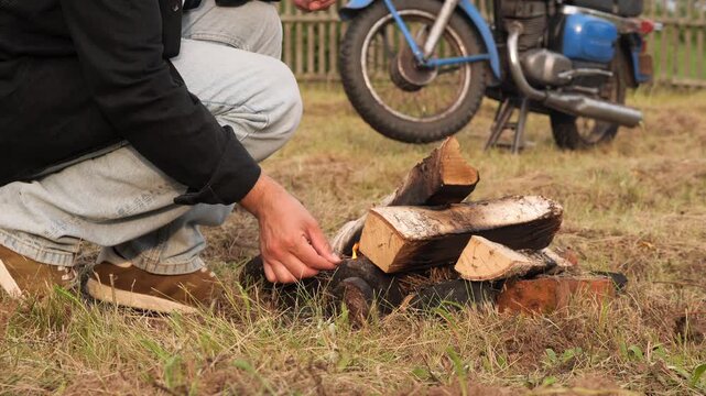 Biker lighting campfire after motorcycle trip near fence