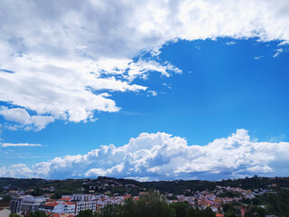 Vibrant vista featuring a bright blue sky punctuated by fluffy white clouds over a hillside village. Represents serenity, tranquility, and a connection to nature.