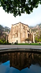 Obraz premium A grand stone edifice reflects in a still pool, framed by foliage and mountains