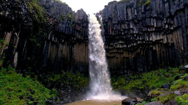 Hengifoss waterfall plunges into a serene pool surrounded by towering hexagonal basalt formations in Iceland wild landscape. This captivating site embodies the raw beauty of nature.